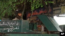 FILE - An Afghan policeman keeps watch on a vehicle at the site of the Park Place Hotel in Kabul, Afghanistan, where gunmen had stormed a guesthouse during a party for foreigners, May 13, 2015.