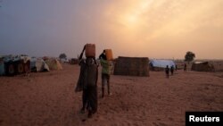 FILE - Sudanese people who fled the conflict in Sudan's Darfur region, carry their jerrycans of water as they walk toward their makeshift shelters in Adre, Chad July 21, 2023.