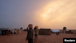 FILE - Sudanese people who fled the conflict in Sudan's Darfur region, carry their jerrycans of water as they walk toward their makeshift shelters in Adre, Chad on July 21, 2023.