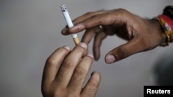 FILE - A man passes a cigarette to another as they sit on a pavement along a road in New Delhi, India, Aug. 18, 2015. 