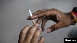 FILE - A man passes a cigarette to another as they sit on a pavement along a road in New Delhi, India, Aug. 18, 2015. 