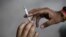 FILE - A man passes a cigarette to another as they sit on a pavement along a road in New Delhi, India, Aug. 18, 2015. 