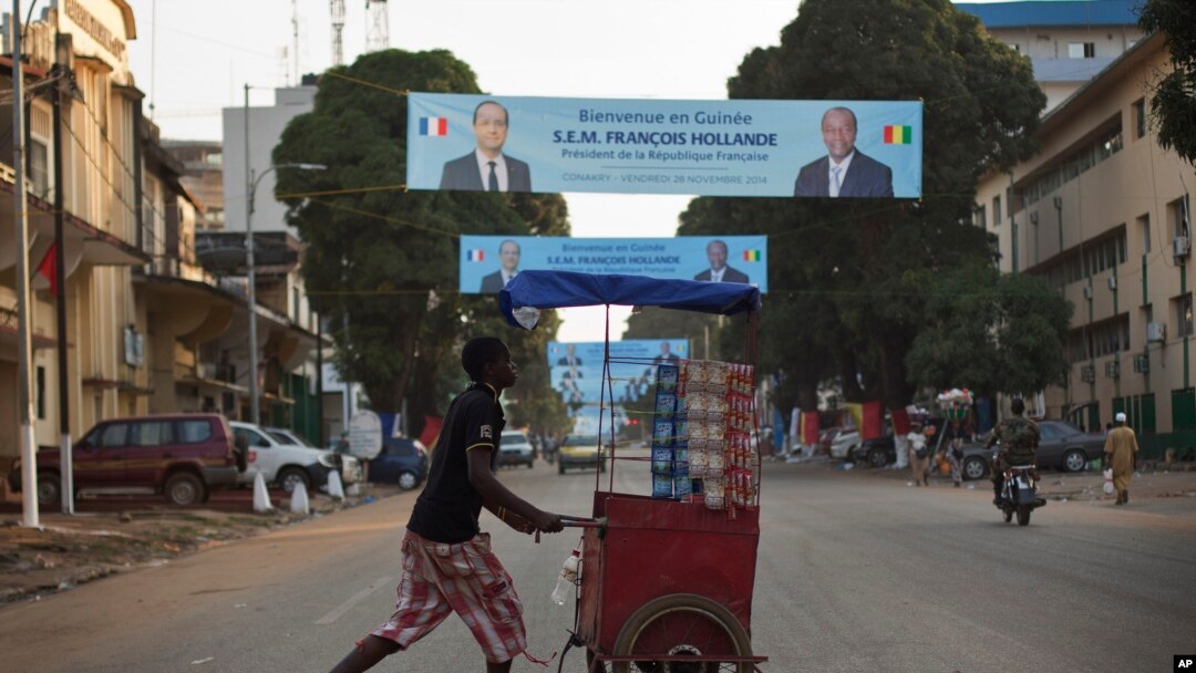 Seorang pedagang kaki lima di Guinea melawati sebuah spanduk di jalan yang memperlihatkan gambar Presiden Perancis Hollande dan Presiden Guinea Alpha Conde di Conakry, Guinea (26/11/2014). 