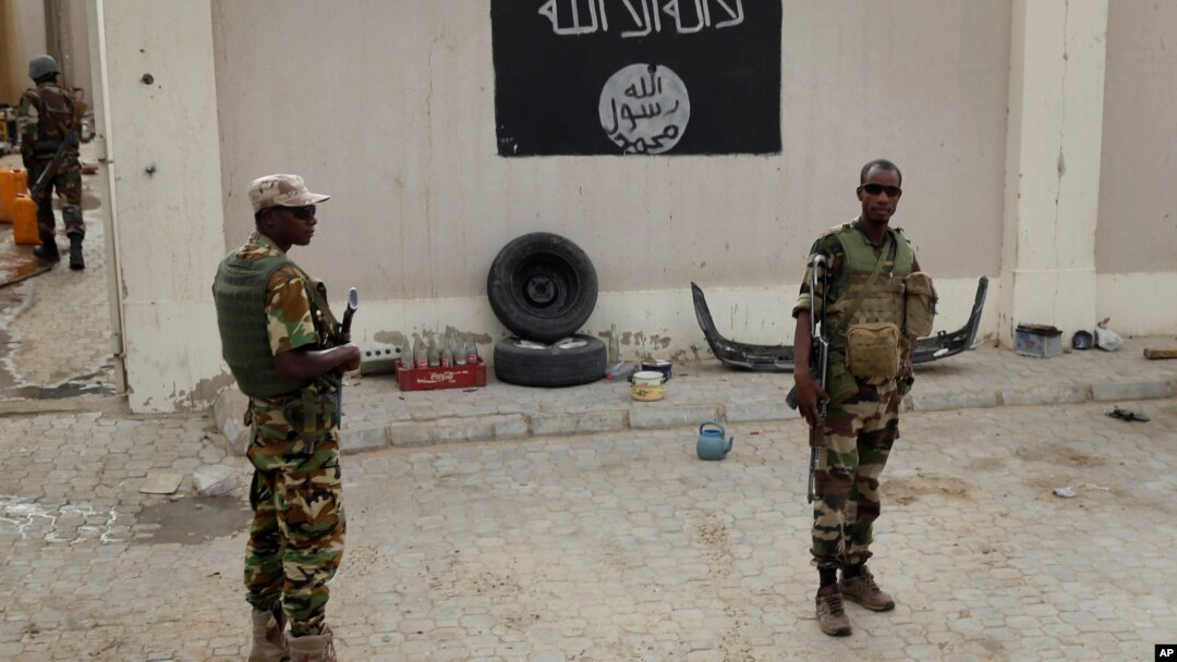 Chadian soldiers stand at a checkpoint in front of a Boko Haram flag in the Nigerian city of Damasak, March 18, 2015.
