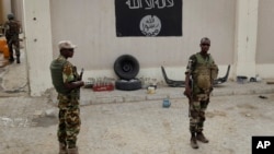 Chadian soldiers stand at a checkpoint in front of a Boko Haram flag in the Nigerian city of Damasak, March 18, 2015.