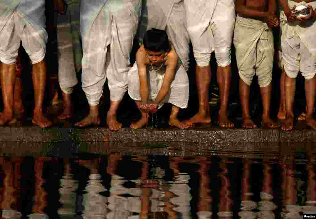 A young devotee grasps water while offering prayers on the banks of the Hanumante River during the Swasthani Brata Katha festival in Bhaktapur, Nepal.