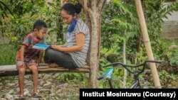 Seorang ibu dan anak yang sedang membaca booklet informasi Virus Corona di Desa Kilo, Kecamatan Poso Pesisir, Kabupaten Poso, Sulawesi Tengah, 30 Maret 2020. (Foto: Institut Mosintuwu)