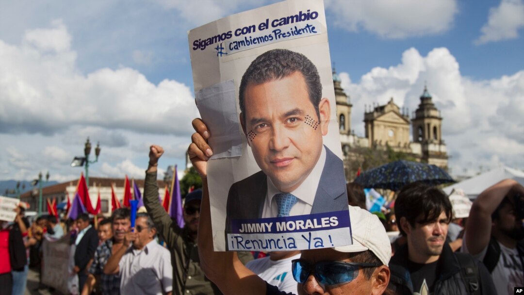 A man holds up a campaign poster of Guatemala's President Jimmy Morales during a gathering to show support for the Commissioner of the United Nations International Commission Against Impunity, Ivan Velasquez in Guatemala City, Saturday, Aug. 26, 2017. 