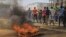 Protesters walk past a burning tyre in the Eastern Congolese town of Beni, Friday Dec. 28, 2018, as they demonstrate against the election postponed until March 2019, announced by Congo's electoral commission for Beni residents that is blamed on a deadly Ebola outbreak. 