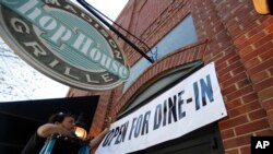 Jason Godbey hangs a banner over the entrance of Madison Chop House Grille as they prepare to shift from take out only to dine-in service, April 27, 2020, in Madison, Ga. Gov.