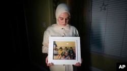 FILE - Maryam Kamalmaz holds a photo of her father, Majd Kamalmaz, with some of his 14 grandchildren in Grand Prairie, Texas, Jan. 17, 2024. The Syrian-born American psychotherapist died while being held in Syria. His family has filed a lawsuit against the Syrian government.