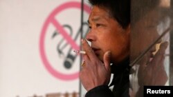 A man smokes in front of a "no smoking" sign outside a shopping mall in Shanghai, Jan. 10, 2014.