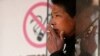 FILE - A man smokes in front of a "no smoking" sign outside a shopping mall in Shanghai, Jan. 10, 2014.