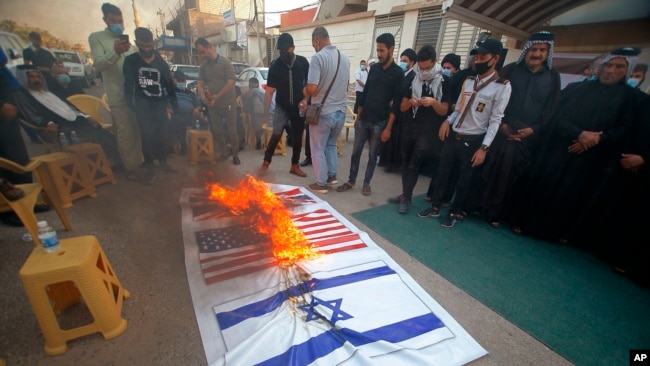 FILE - Supporters of the Iran-backed Kataeb Hezbollah militia burn representations of Israeli, U.S. and British flags during a protest against the United Arab Emirates and Bahraini normalization agreement with Israel in Najaf, Iraq, September 18, 2020