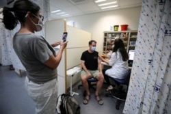 A woman takes a picture of a man as he receives a third shot of the coronavirus disease (COVID-19) vaccine as country launches booster shots for over 40-year-olds, in Jerusalem August 20, 2021. (REUTERS/Ammar Awad)