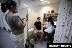 Woman takes photo of man as he receives third injection of coronavirus disease (COVID-19) vaccine as country launches booster shots for those over 40, in Jerusalem on August 20 2021. (REUTERS / Ammar Awad)