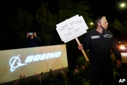 A Boeing worker wears a mask while holding a "Happy Strike Day" sign after union members voted overwhelmingly to reject a contract offer and go on strike Sept. 13, 2024, outside the company's factory in Renton, Washington.