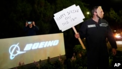 A Boeing worker wears a mask while holding a 'Happy Strike Day' sign after union members voted overwhelmingly to reject a contract offer and go on strike Sept. 13, 2024, outside the company's factory in Renton, Wash.