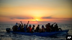 FILE: Migrants from Tunisia gesture as they sail in a wooden boat as they are assisted by crew members of the Spanish NGO Open Arms, sixteen miles west of the Italian island of Pantelleria in the Mediterranean sea, on Friday, Aug. 5, 2022. 