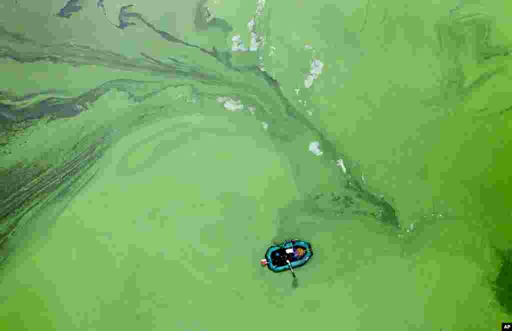 A fisherman in a rubber boat is surrounded by rotting cyanobacteria in the Kyiv Water Reservoir near Kyiv, Ukraine.
