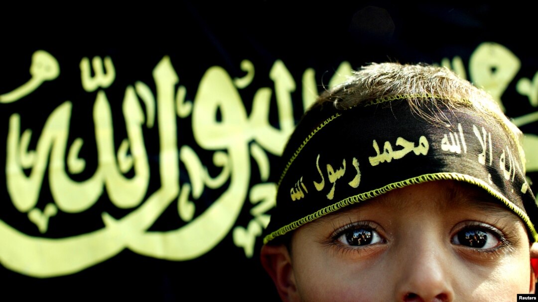 Arhiva - Dečak stoji ispred zastave Islamskog džijada. Mnoge zapadne zemlje zaziru od toga da Islamska država, nakon gubitka teritorija, aktivno nastavlja da regrutuje pristalice i po evropskim zemljama, uključujući i decu.