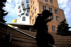In this Tuesday, July 16, 2019 photo a passer-by appears in silhouette while walking past the Ray and Maria Stata Center, behind, on the campus of Massachusetts Institute of Technology, in Cambridge, Mass.