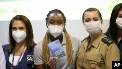 La sprinteuse Rosangela Santos, au centre, montre son certificat de vaccination après avoir reçu une injection du vaccin anti covid Pfizer à Rio de Janeiro, Brésil, le vendredi 14 mai 2021, avant les Jeux Olympiques de Tokyo en juillet. (Photo AP/Silvia Izquierdo)