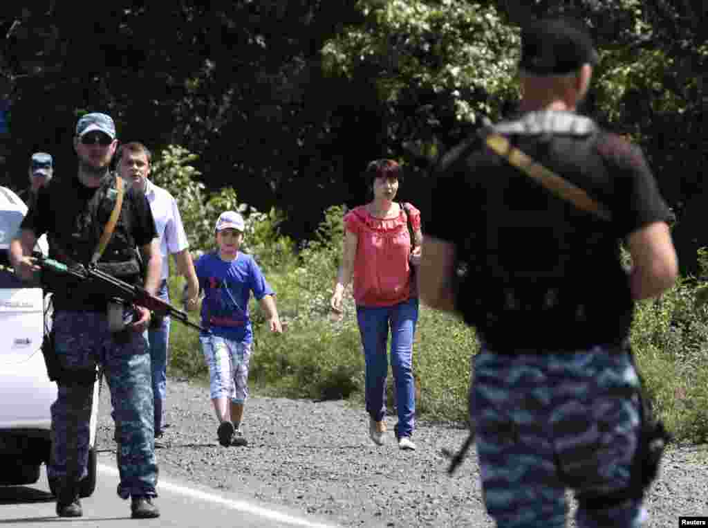 Local residents walk past armed pro-Russian separatists as they flee from what they say was shelling by Ukrainian forces, in the suburbs of Shakhtarsk, Donetsk region, July 28, 2014.
