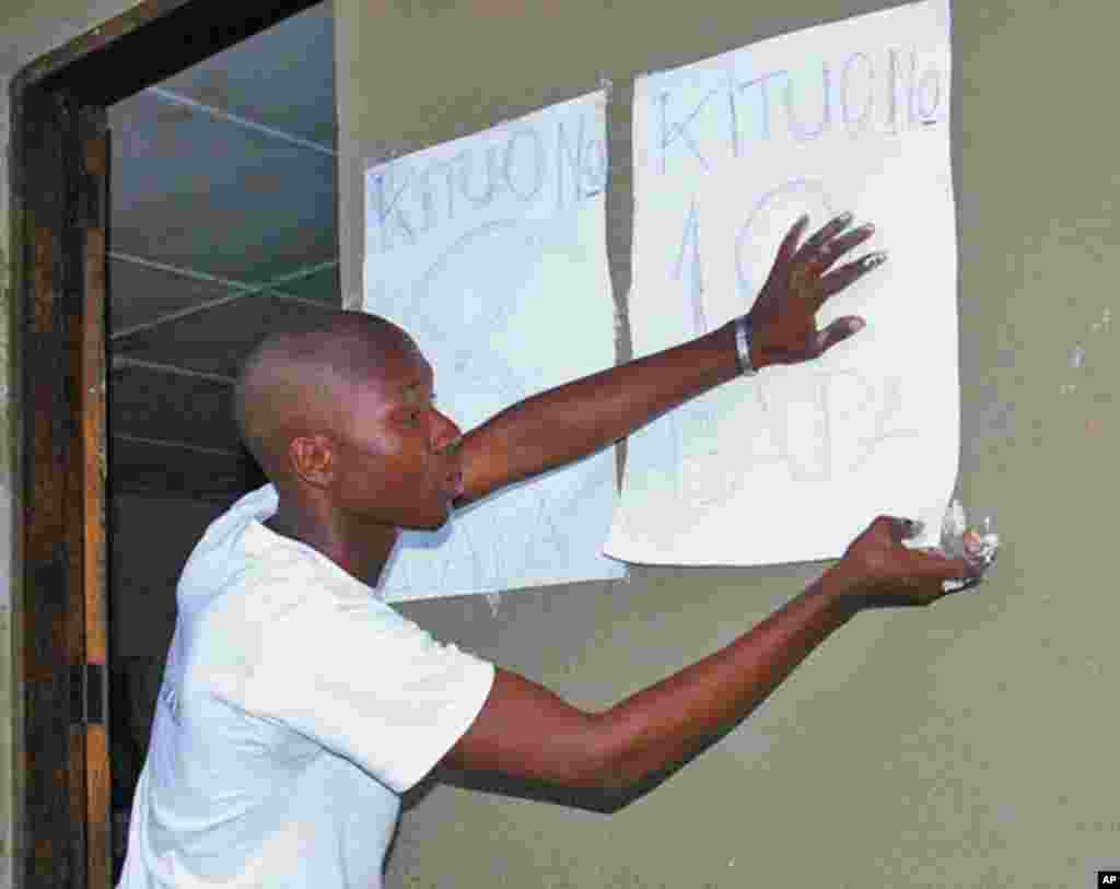 Mfanyakazi wa kituo cha uchaguzi akibandika tangazo la kituo cha Madatu huko Gongolamboto