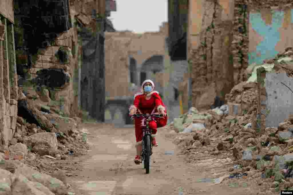 An Iraqi woman, dressed as Santa claus, rides her bicycle in the old city of Mosul.