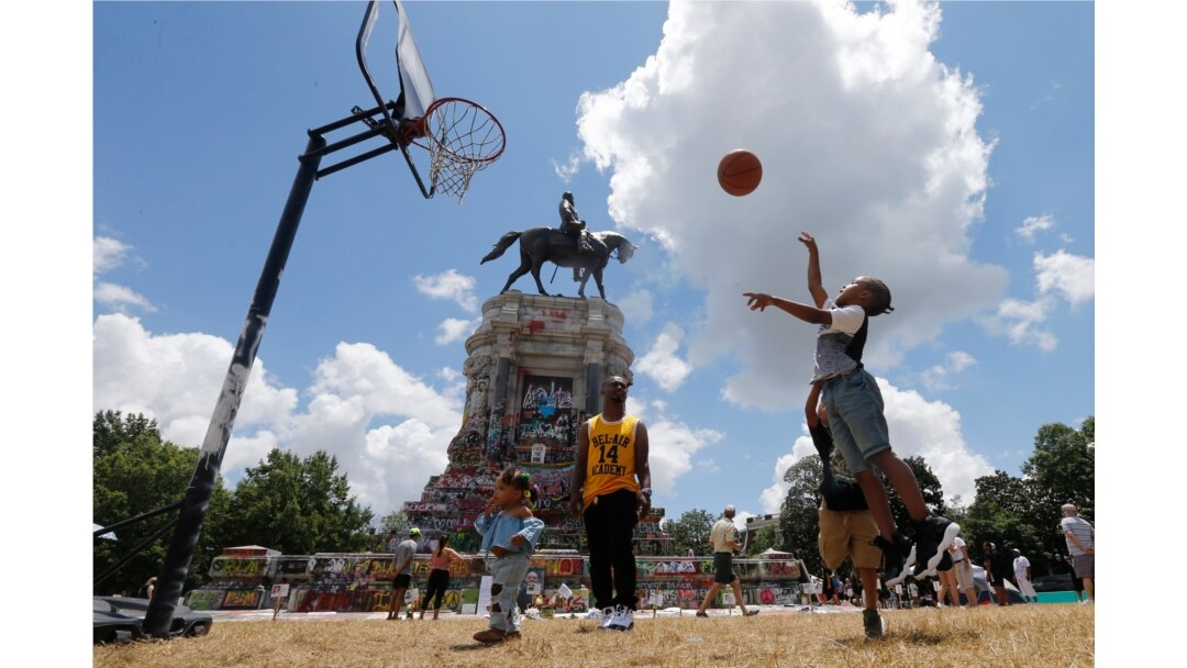 Isaiah Bowen, right, takes a shot as his dad, Garth Bowen, center, looks on at a basketball hoop in front of the statue of Confederate General Robert E. Lee on Monument Avenue in Richmond, Virginia, June 21, 2020.