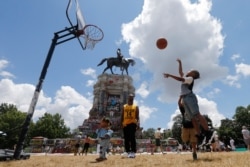 Isaiah Bowen, right, takes a shot as his dad, Garth Bowen, center, looks on at a basketball hoop in front of the statue of Confederate General Robert E. Lee on Monument Avenue in Richmond, Virginia, June 21, 2020.