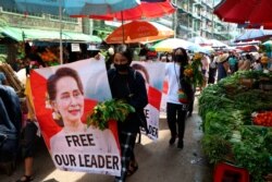 FILE - Anti-coup protesters walk through a market with images of ousted Myanmar leader Aung San Suu Kyi at Kamayut township in Yangon, Myanmar, April 8, 2021.