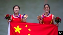 Atlet dayung putri China, Zou Jiaqi (kiri) dan Qiu Xiuping berfoto dengan medali emas dari final dayung ganda putri kelas ringan dalam Asian Games di Hangzhou, China, Minggu, 24 September 2023. Mereka menyumbang medali emas pertama untuk China. (Foto: Louise Delmotte/AP Photo)