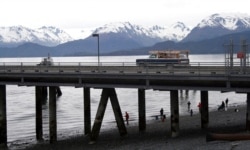 FILE - A vehicle drives on a pier to be loaded onto an Alaska state ferry while people fish underneath in Homer, Alaska, May 24, 2015. The U.S. Supreme Court will hear arguments April 19, 2021, in a case involving federal virus relief for tribes.