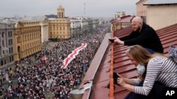 مردم در حال عکاسی از تظاهرکنندگان در حال حمل پرچم ملی باستانی بلاروس در مسیر حرکت به سوی میدان استقلال در مینسک. ۲۳ اوت ۲۰۲۰