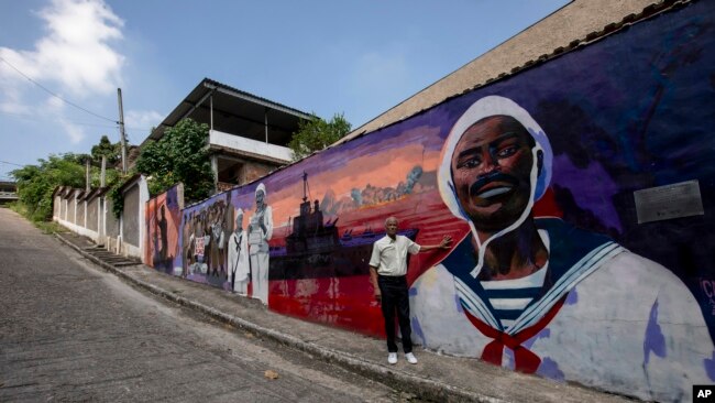 FILE - Adalberto Cândido poses for a photo in front of a mural that depicts the story of his father João Cândido, a black sailor who led a revolt against the Brazilian Navy, in Sao Joao de Meriti, Rio de Janeiro state, Brazil, December 21, 2023.