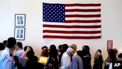 FILE - People file past the U.S. flag and a portrait of President Barack Obama on their way to attend a naturalization ceremony in Irving, Texas, July 3, 2014. 