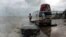FILE - Tourists pose next to the Southernmost Point marker as large waves crash on the sea wall, July 8, 2005, in Key West, Fla., as winds from Hurricane Dennis stir up sand and surf. 