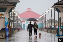 FILE - A couple walk in the rain with their dog along the Huntington Beach Pier in Huntington Beach, Calif., on Feb. 6, 2024. (AP Photo/Marcio Jose Sanchez, File)