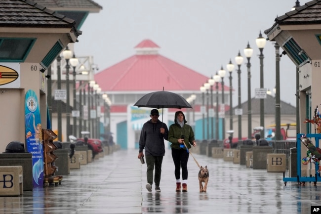 FILE - A couple walk in the rain with their dog along the Huntington Beach Pier in Huntington Beach, Calif., on Feb. 6, 2024. (AP Photo/Marcio Jose Sanchez, File)