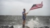 Youtuber Mark Peyton holds a US flag as he poses for his brother Matt Peyton on the shoreline ahead of the arrival of Hurricane Helene in Alligator Point, Florida, on Sept. 26, 2024. 