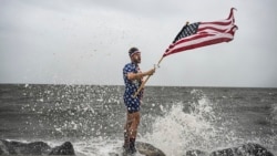 YouTuber Mark Peyton memegang bendera Amerika berpose untuk saudaranya Matt Peyton di tepi pantai, menjelang Badai Helene di Alligator Point, Florida, 26 September 2024.