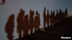 FILE - Asylum-seeking migrant families cast shadows on a wall as they form a queue to be processed by the U.S. Border Patrol after crossing the Rio Grande into the United States from Mexico in Roma, Texas, Aug. 12, 2021.