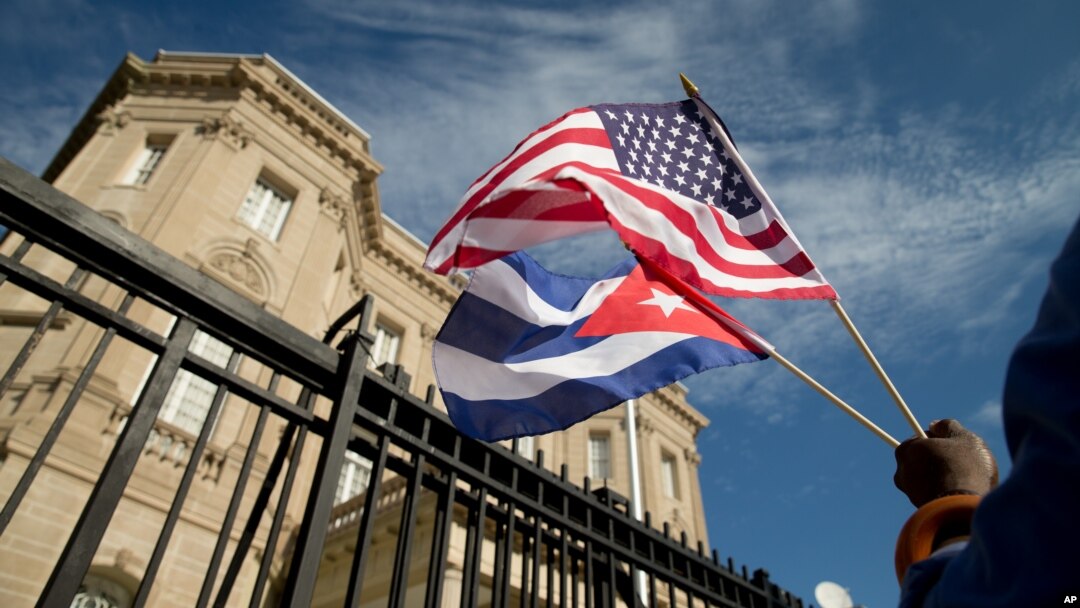 Một người Mỹ gốc Cuba cầm cờ Cuba và cờ Mỹ đứng trước đại sứ quán Cuba mới được mở lại tại Washington, Mỹ, hôm 20/7/2015. 