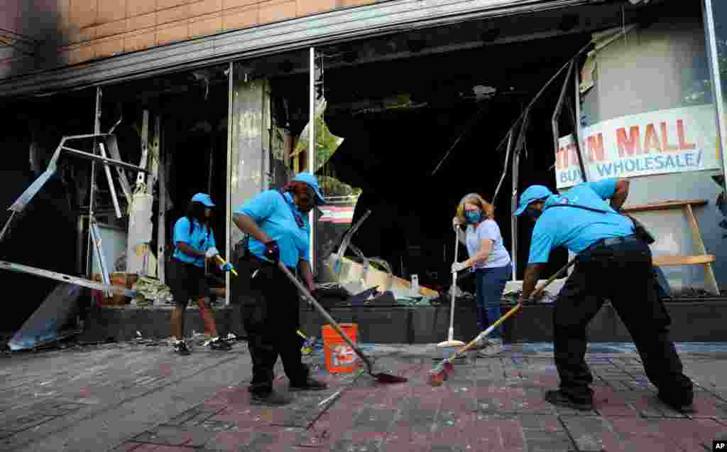 Workers and a volunteer clean up damage outside a burned-out clothing store in Birmingham, Alabama, June 1, 2020, following a night of unrest. 