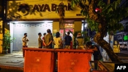 FILE - A woman searches for salvageable items from a rubbish bin, as people queue to use a bank's automated teller machine, in the downtown area of Yangon, April 9, 2021, as the country remains in turmoil after the February military coup. 