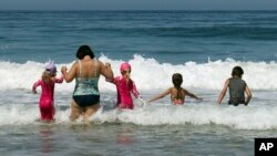 A woman and children wade into the surf in Hermosa Beach, Calif., as a record-setting heat wave hit Southern California, July 6, 2018. Records for high temperatures for the date were being set all over the region, some before noon, with many in triple digits.