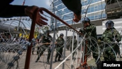 Thai soldiers set up a barbed-wire fence at the Government's temporary headquarters as farmer protesters gather outside in Bangkok on February 10, 2014. 