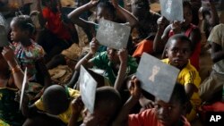 FILE - Children show their drawings to the teacher in a school set in the Mpoko refugee camp near the airport in Bangui, Central African Republic, Feb. 15, 2016. 